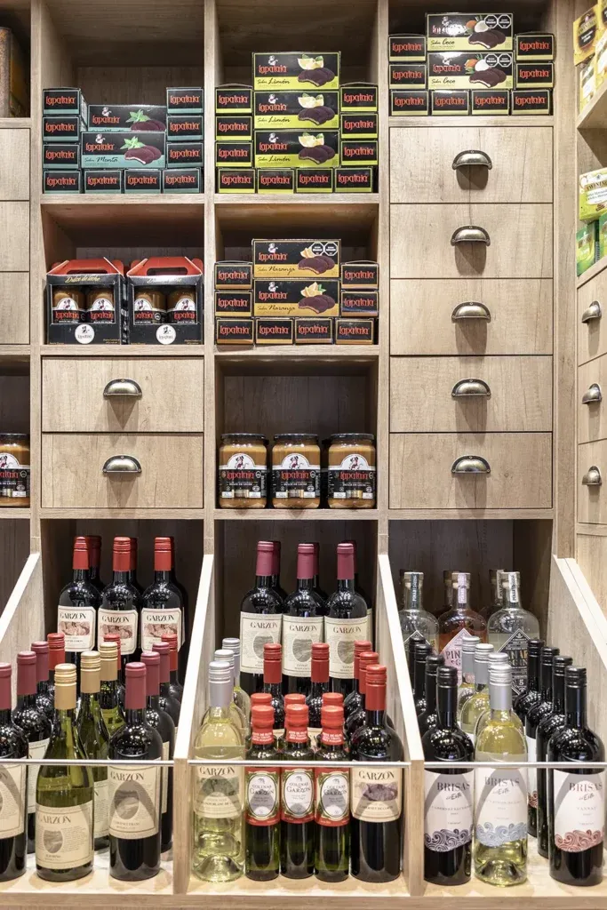 Estantería de madera clara del almacén con alfajores, dulces y vinos uruguayos.