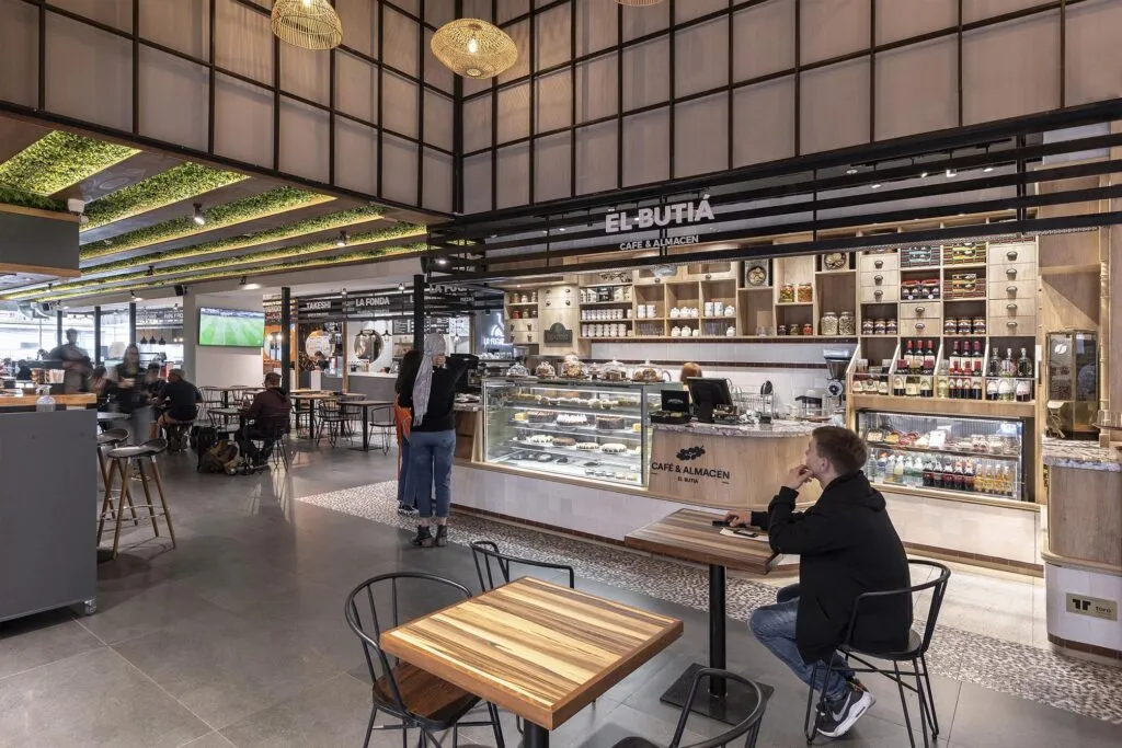 Local de El Butiá en una plaza de comidas, con mesas de madera, clientes sentados y la estantería del almacén al fondo.